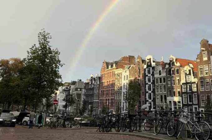 Double rainbow over traditional canal houses and bicycles in Amsterdam, Netherlands, during a sunny rain shower.