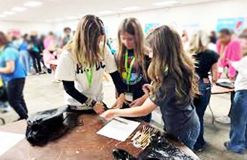 Three girls standing in front of a table.